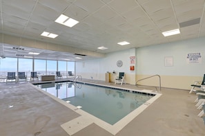 Una piscina interior con paneles de techo transparentes, señales de salida de emergencia y vistas al exterior a través de amplios ventanales.