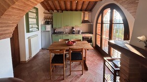 A rustic kitchen with green cabinets, a wooden table, and a large arched window.