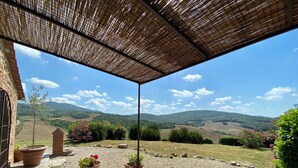 An outdoor patio with a table and chairs, surrounded by potted plants and a view of rolling hills.
