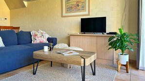Un salon avec un canapé bleu, une table basse, un téléviseur posé sur un meuble en bois, un tableau accroché au mur et une plante en pot.