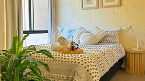 Une chambre à coucher avec un lit, un ventilateur de plafond, une fenêtre avec des rideaux, une plante en pot et des tableaux encadrés accrochés au mur.