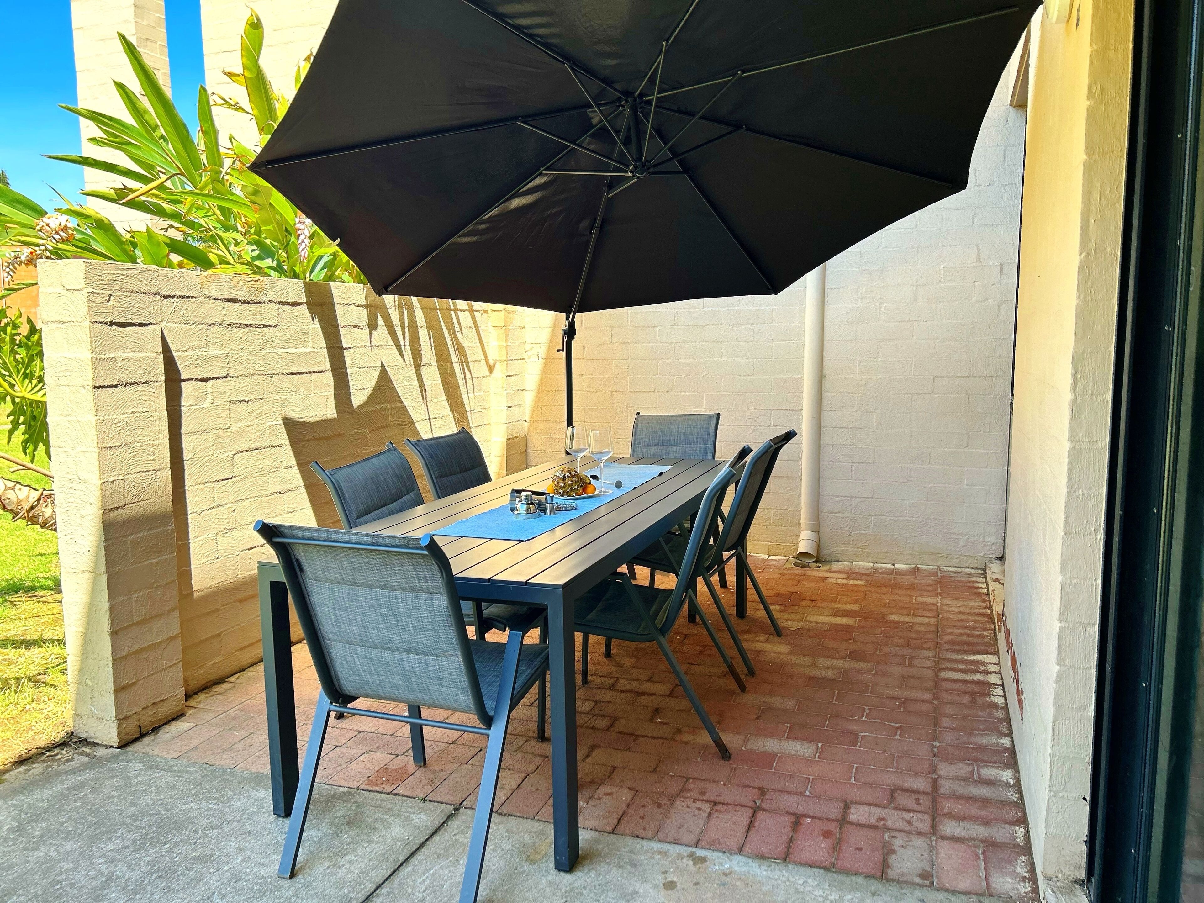 Un patio al aire libre con una mesa, sillas y un gran paraguas, junto a una pared de ladrillo.