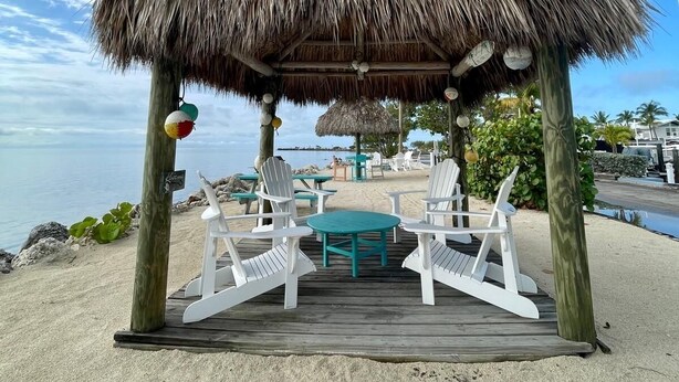A beachside gazebo with a thatched roof, white chairs, and a small table. - Refined. Safe. Clean. Waterfront. Golf cart , courtesy to our guests (Key Largo)