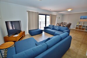 Relax in this stylish living room with a large sofa, flat-screen TV, and sliding glass door leading to a balcony.