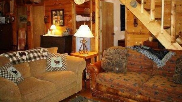 Un salon chaleureux avec un escalier en bois, un canapé et une lampe.