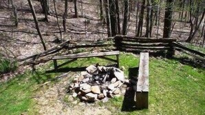 Un banc en bois rustique, installé près d’un foyer en pierre, dans une clairière au cœur de la forêt.