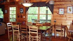 L’intérieur d’un chalet en bois, avec une table et des chaises, de grandes fenêtres et des paniers suspendus.