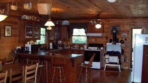 L’intérieur d’un chalet rustique comprend un coin repas en bois, des tabourets de bar, une cuisine équipée d’une cuisinière et d’un réfrigérateur, ainsi que des paniers suspendus.
