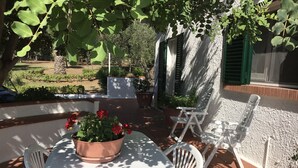 En terrasse med et hvidt bord og stole, en potteplante med røde blomster og en pergola med grønne blade.