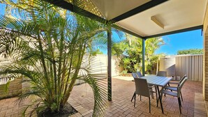 En overdækket terrasse med et bord og stole, omgivet af plantekasser og et flisebelagt gulv.
