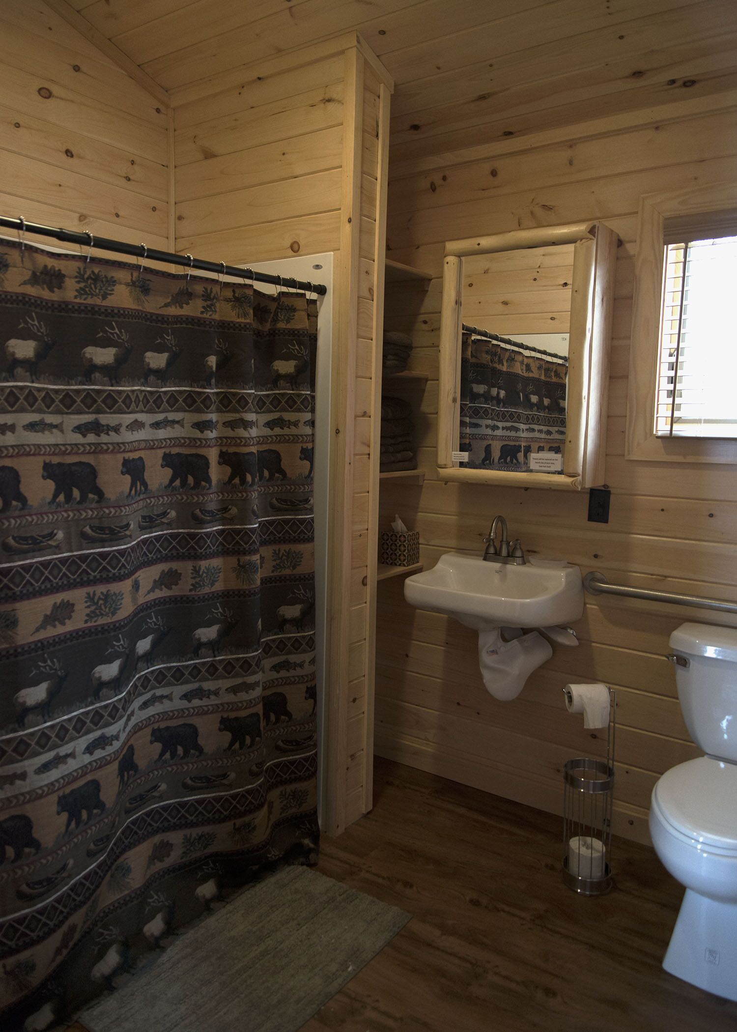 A wooden cabin bathroom with a shower curtain featuring animal prints, a sink, and a toilet.