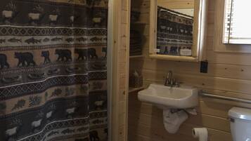 A wooden cabin bathroom with a shower curtain featuring animal prints, a sink, and a toilet.