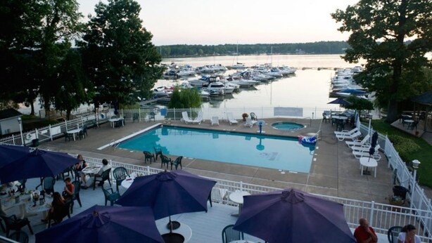 A pool area with lounge chairs and umbrellas, surrounded by a marina with boats.