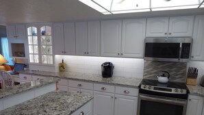 A modern kitchen with white cabinets, granite countertops, a stainless steel oven, and a microwave. - BEACHSIDE Paradise: 3BR Condo with Heated Pool - Steps to Cocoa Beach Pier! (Cocoa Beach)