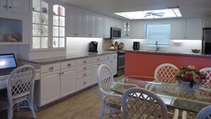 A modern kitchen with white cabinets, a glass-top dining table, wicker chairs, and a built-in microwave. - BEACHSIDE Paradise: 3BR Condo with Heated Pool - Steps to Cocoa Beach Pier! (Cocoa Beach)