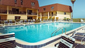 A swimming pool with lounge chairs and a building with balconies. - BEACHSIDE Paradise: 3BR Condo with Heated Pool - Steps to Cocoa Beach Pier! (Cocoa Beach)