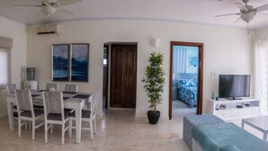 A modern living room with a dining area, a TV, and a ceiling fan. - Beautiful 2 bedroom 2 bath in a beachfront community (Punta Cana)