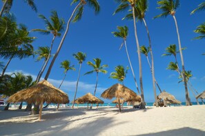 Ein Strand mit Palmen und strohgedeckten Sonnenschirmen.