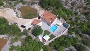 An aerial view of a house with a swimming pool, a tennis court, and a garden.