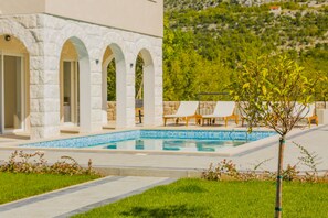 A poolside area with a stone building, outdoor seating, and a view of a hillside. - family-friendly, capacity 6+2 (Zagvozd)
