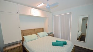 Quarto com cama, mesas de cabeceira, ventilador de teto e espelho.