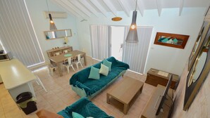 Uma sala de estar ampla com um sofá verde-água, mesa de centro de madeira e mesa de jantar com cadeiras.