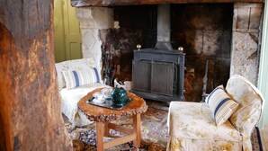 A cozy room with a stone fireplace, two upholstered chairs, a small wooden table with a tray, and a patterned rug.