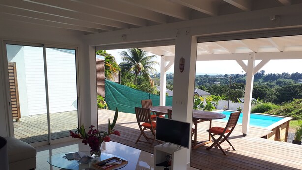 Una sala de estar moderna con una mesa de centro de vidrio, un televisor y un comedor con vista a la piscina.