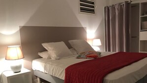 Un dormitorio moderno con una cama, lámparas de noche, una manta roja y una mesita de noche blanca.