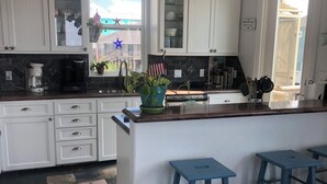 Eine Küche mit weißen Schränken, einer großen Kochinsel mit Sitzgelegenheiten, einer Kaffeemaschine und einer Pendelleuchte.