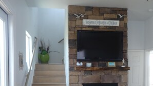 Eine Treppe führt zu einem Wohnbereich mit Kamin aus Stein, einem Flachbildfernseher und einem Schild darüber.