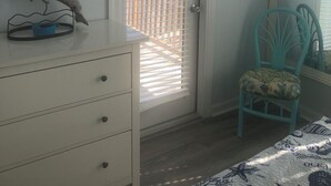 Ein Zimmer mit einem weißen Kommode, einem türkisgrünen Sessel, einem an der Wand montierten Fernseher und einer Tür mit Jalousien.