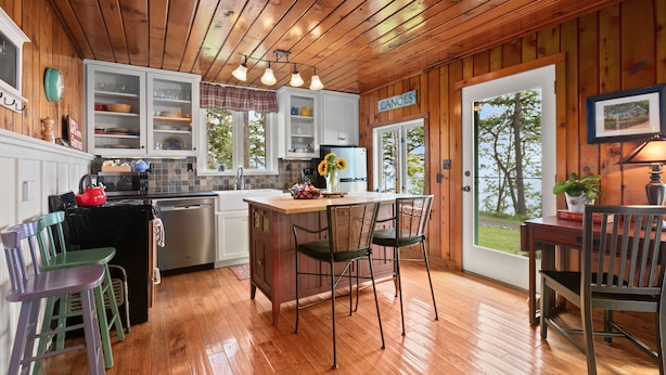 A wooden interior with a kitchen island, bar stools, and a view of the outdoors.