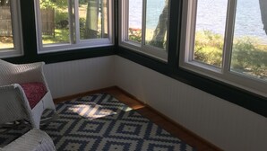 A corner room with a view of a lake, a patterned rug, and a white chair with red cushions. - Beautiful Views @ 4-Season Lake House, Private Sandy Beach (Fryeburg)