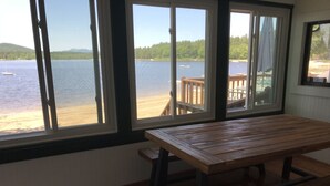 A room with a wooden table and bench, large windows with a view of a lake and dock. - Beautiful Views @ 4-Season Lake House, Private Sandy Beach (Fryeburg)