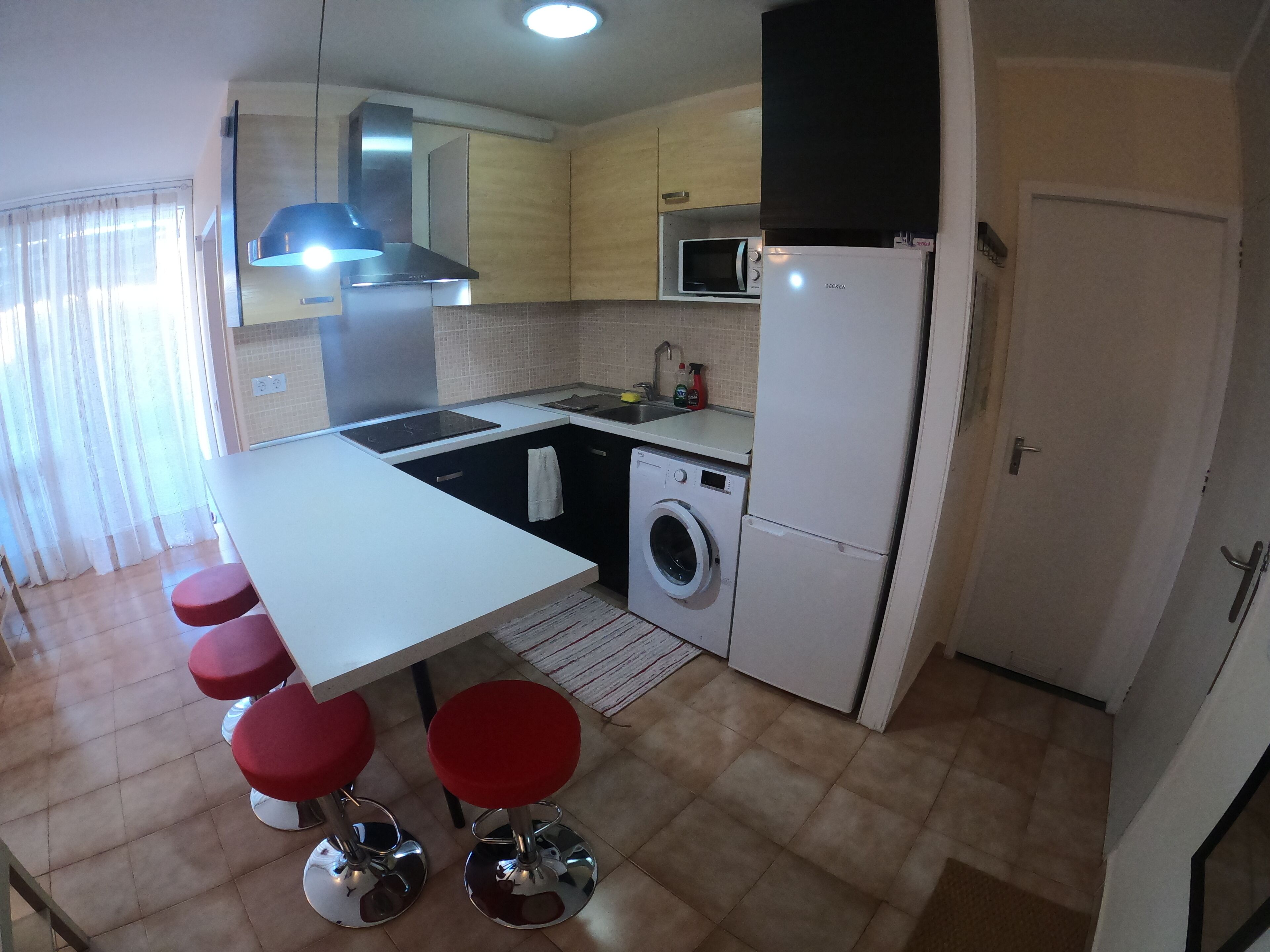 Una cocina compacta con una isla central, lavadora, microondas y refrigerador.