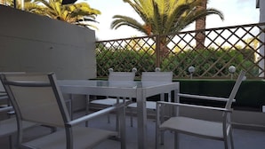 An outdoor patio with a table and chairs, surrounded by a lattice fence and palm trees. - Spring Apartment  (Costa del Silencio)