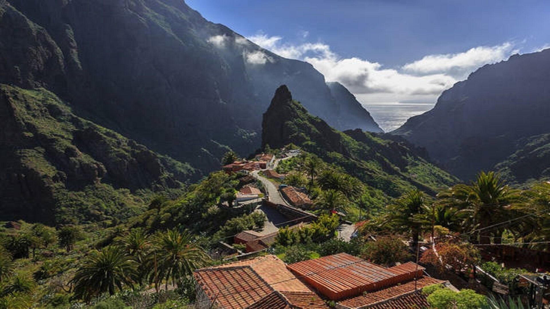 Un paisaje montañoso con una carretera sinuosa, casas escalonadas y vegetación exuberante.