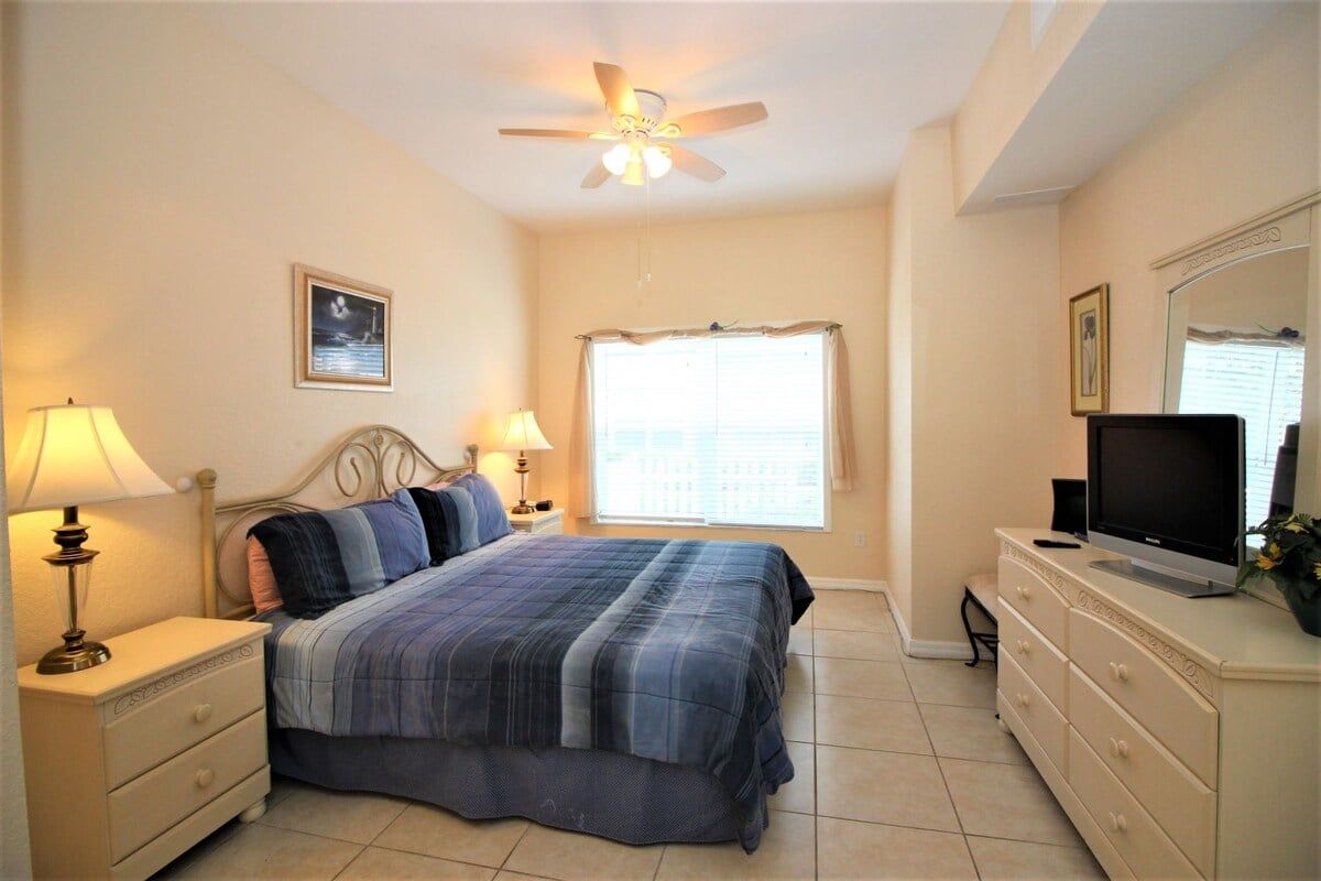 A bedroom with a bed, nightstands, a television, and a ceiling fan.