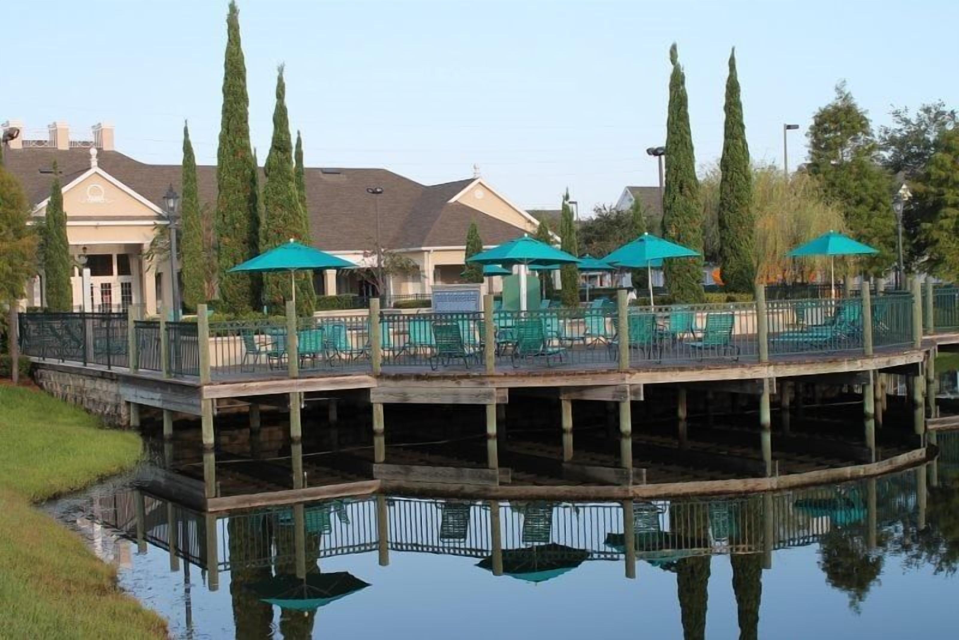 A waterfront restaurant with outdoor seating, a dock, and a reflection in the water.