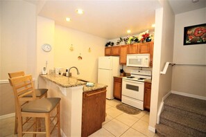 A compact kitchen with a refrigerator, microwave, stove, and wooden cabinets. - Cozy Home Away From Home - VB010 (Kissimmee)