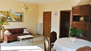 A living room with a brown sofa, a white coffee table, and a dining table with a white tablecloth. There is a wooden cabinet and a plant on the table. - "FARFALLA" HOLIDAY HOUSE with PANORAMIC VIEW on LAKE MAGGIORE (Cannobio)