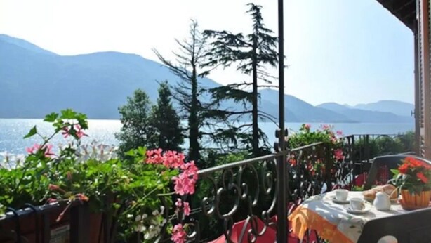 A balcony with a view of a lake and mountains, adorned with potted plants and flowers. - "FARFALLA" HOLIDAY HOUSE with PANORAMIC VIEW on LAKE MAGGIORE (Cannobio)