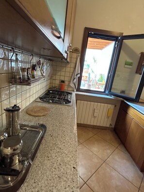 A kitchen with a gas stove, a coffee maker, and a window with a view of the outside. - Villa in Lecce (Lecce)