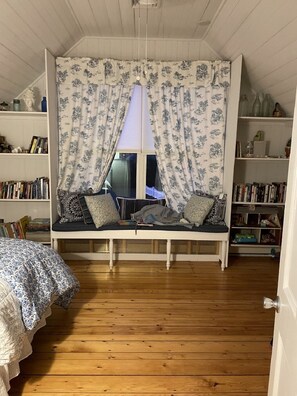 Ein gemütliches Zimmer mit einer eingebauten Sitzbank, Holzboden und Bücherregalen voller Bücher.