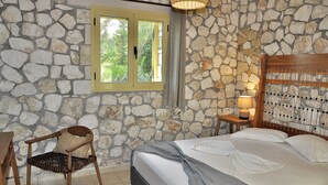 Une chambre avec un mur en pierre, un lit recouvert de draps blancs, une chaise en bois et une petite table avec une lampe.