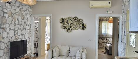 A living room with a stone wall, a flat-screen TV, a white sofa, and a wall-mounted decorative plate.