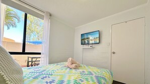 Une chambre à coucher avec un lit, un téléviseur fixé au mur et une fenêtre avec des rideaux.
