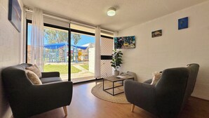 Un salon moderne avec deux canapés sombres, une table basse et une grande porte-fenêtre coulissante donnant sur un espace de jeux extérieur.