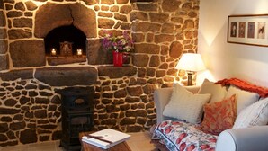 Una sala de estar acogedora con chimenea de piedra, un sofá con cojines estampados, una mesa de centro de madera y un jarrón rojo con flores.
